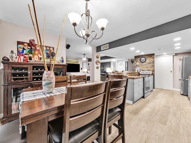 dining area featuring ceiling fan with notable chandelier and light hardwood / wood-style floors