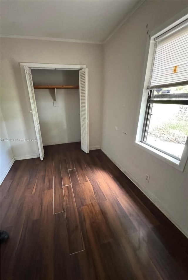 unfurnished bedroom with crown molding, a closet, and dark wood-type flooring