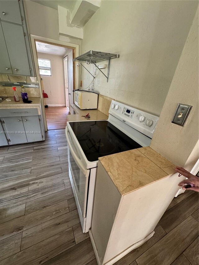 kitchen featuring light wood-type flooring, white electric range, and backsplash