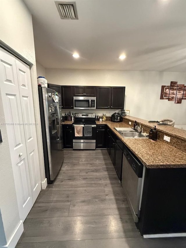 kitchen with kitchen peninsula, appliances with stainless steel finishes, dark stone counters, sink, and wood-type flooring