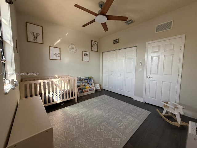 bedroom with ceiling fan, dark hardwood / wood-style floors, a crib, and a closet