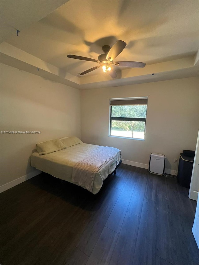 bedroom with ceiling fan, dark hardwood / wood-style flooring, and a tray ceiling