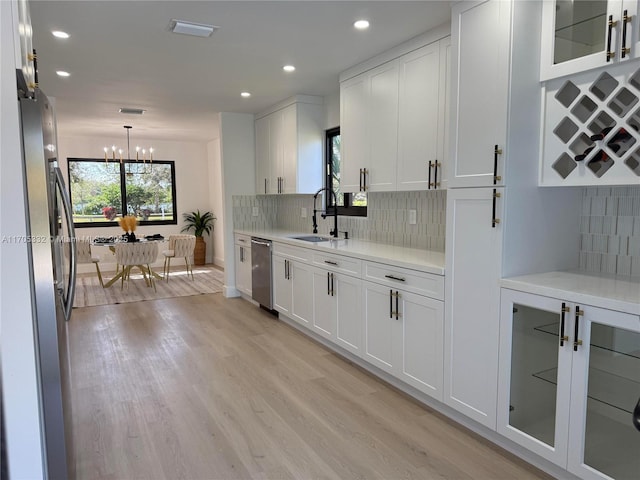 kitchen featuring sink, light wood-type flooring, a notable chandelier, stainless steel appliances, and white cabinets