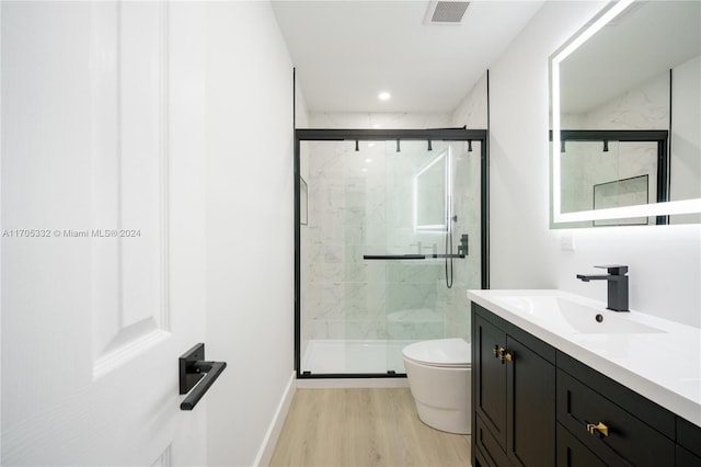 bathroom with a shower with door, vanity, wood-type flooring, and toilet