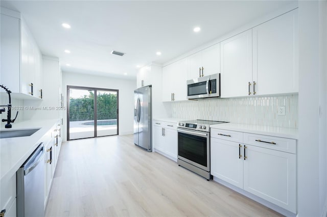 kitchen featuring sink, tasteful backsplash, light wood-type flooring, appliances with stainless steel finishes, and white cabinets