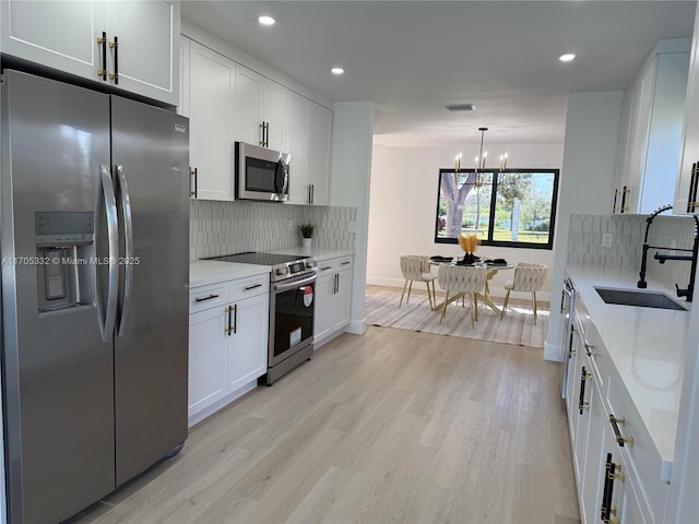 kitchen featuring sink, light stone counters, appliances with stainless steel finishes, light hardwood / wood-style floors, and white cabinets