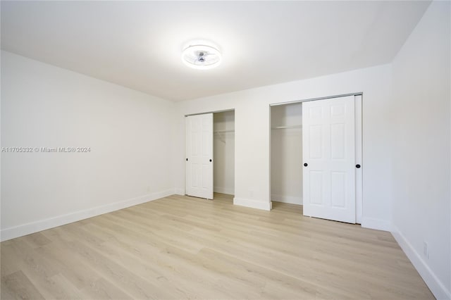 unfurnished bedroom with light hardwood / wood-style floors and multiple closets