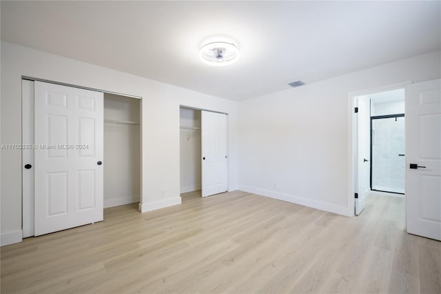 unfurnished bedroom with light hardwood / wood-style floors and two closets