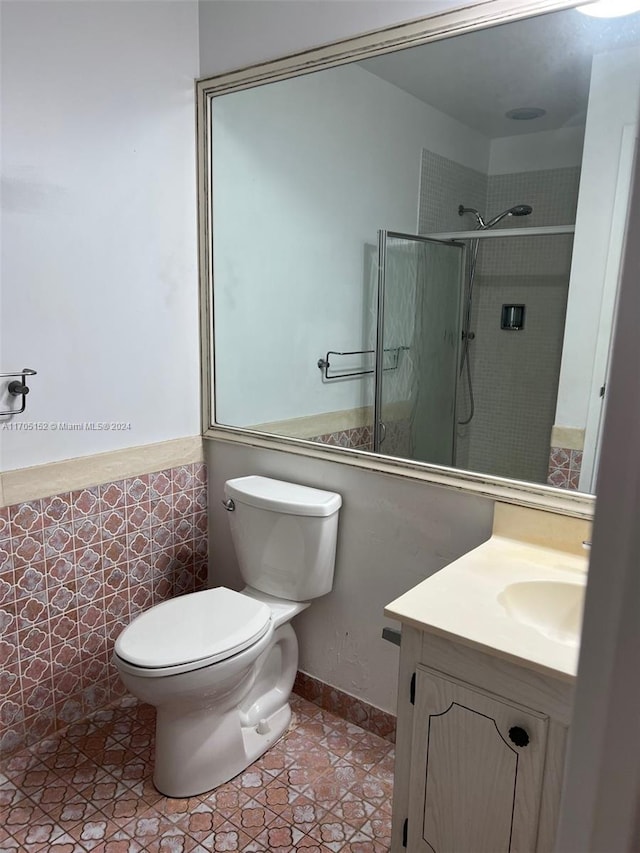 bathroom featuring tile patterned floors, a tile shower, vanity, tile walls, and toilet