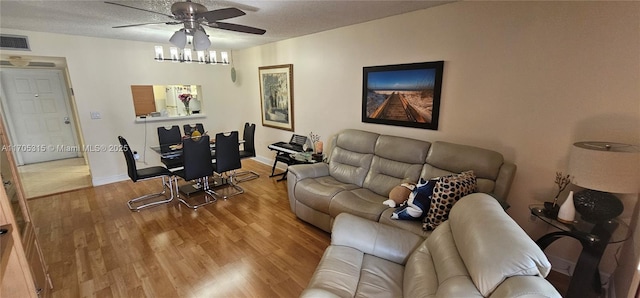 living area featuring a textured ceiling, visible vents, baseboards, a ceiling fan, and light wood finished floors