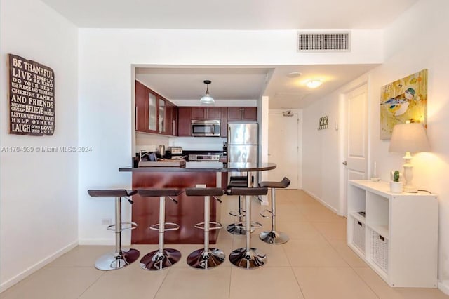 kitchen featuring appliances with stainless steel finishes, light tile patterned floors, hanging light fixtures, and a kitchen breakfast bar