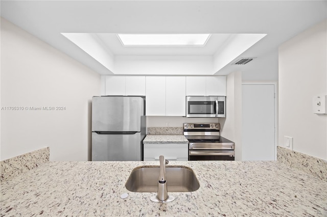 kitchen with light stone counters, stainless steel appliances, a raised ceiling, sink, and white cabinets