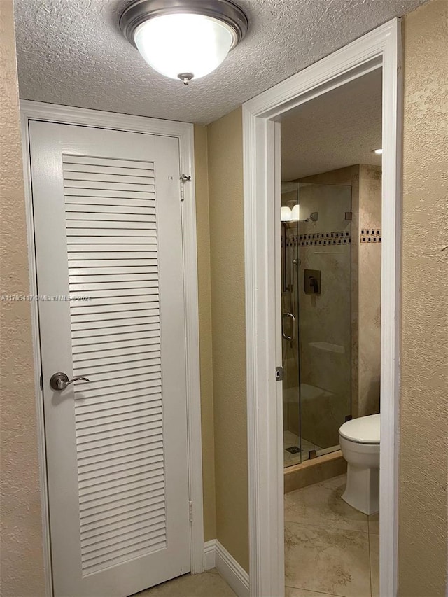 bathroom featuring toilet, a shower with door, a textured ceiling, and tile patterned flooring