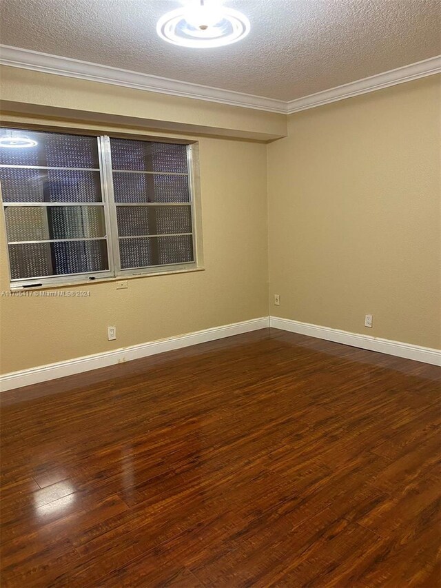 empty room featuring dark hardwood / wood-style floors, ornamental molding, and a textured ceiling