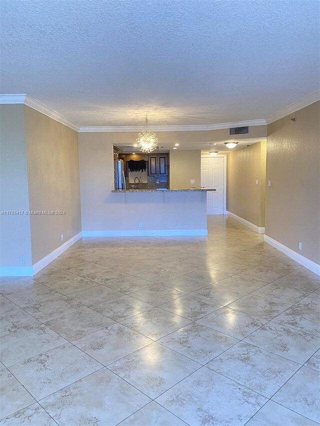 unfurnished living room featuring a notable chandelier, ornamental molding, and a textured ceiling