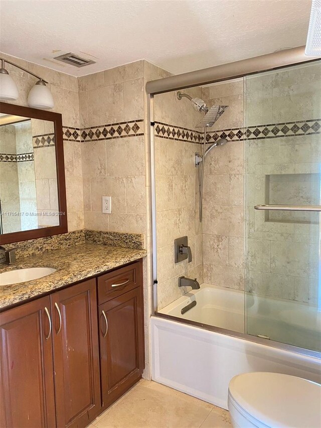 full bathroom with combined bath / shower with glass door, a textured ceiling, vanity, and toilet