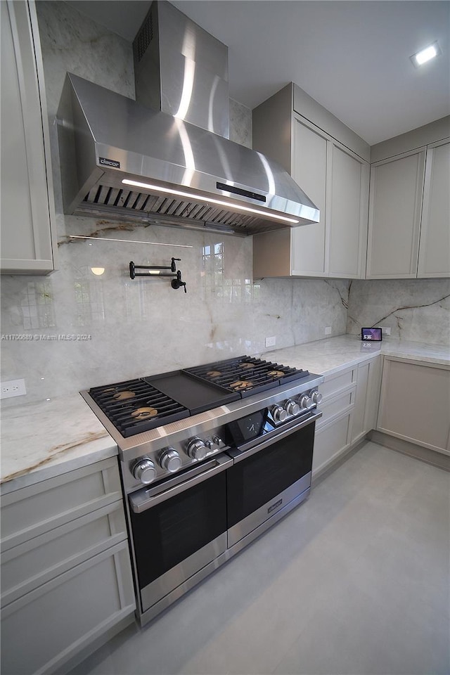 kitchen featuring gray cabinetry, wall chimney exhaust hood, range with two ovens, and light stone counters