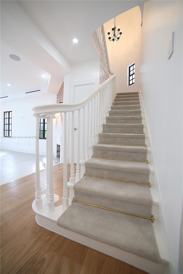 staircase with hardwood / wood-style floors and a chandelier