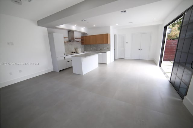 kitchen with white cabinets, sink, wall chimney exhaust hood, decorative backsplash, and a kitchen island