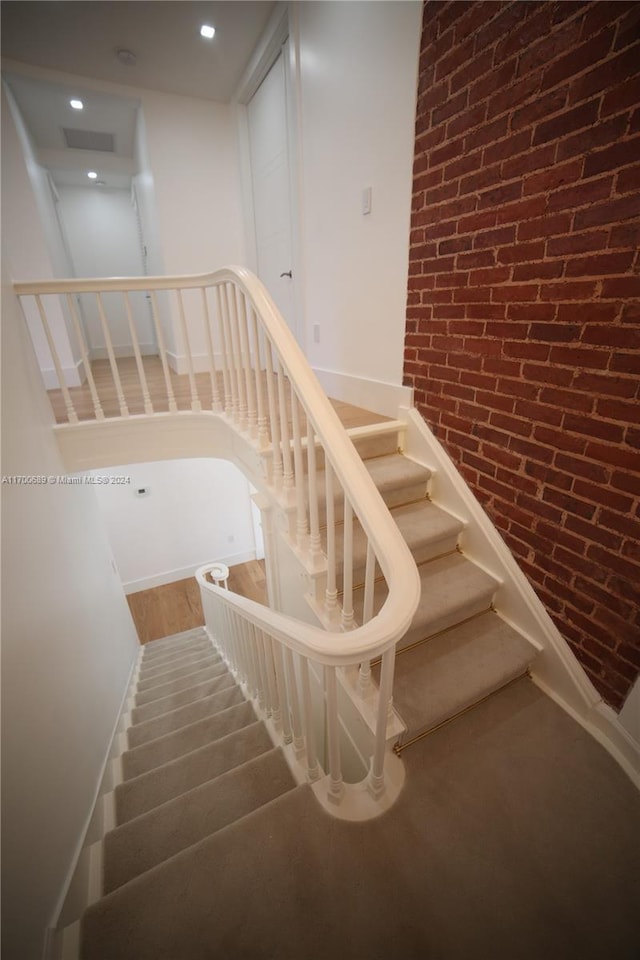 staircase featuring wood-type flooring and brick wall