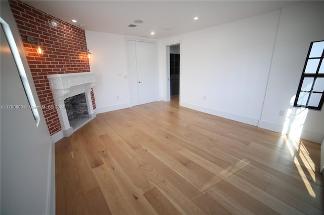 unfurnished living room with a brick fireplace and light hardwood / wood-style flooring