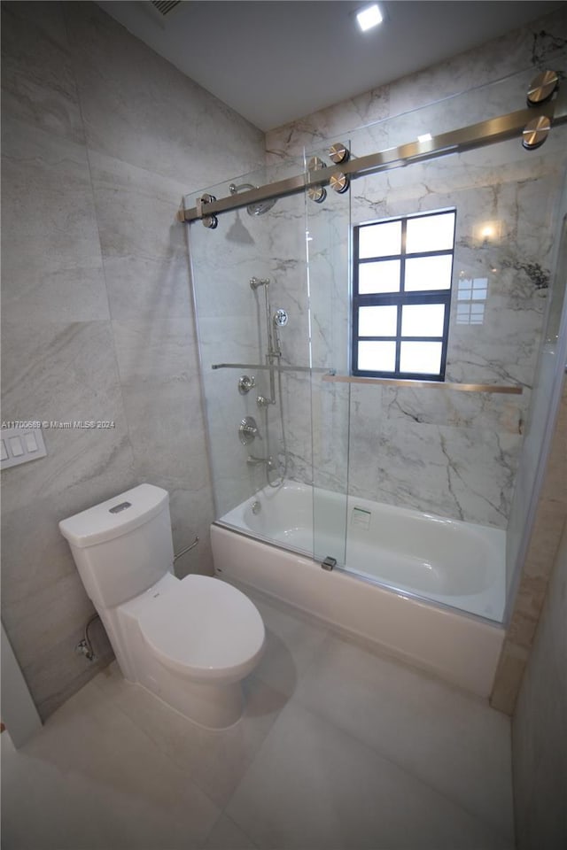 bathroom with tile patterned floors, toilet, tile walls, and combined bath / shower with glass door