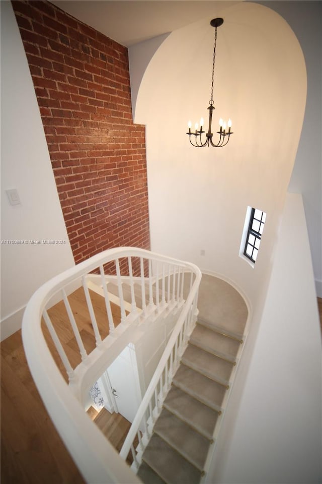 stairway featuring hardwood / wood-style floors, brick wall, and an inviting chandelier