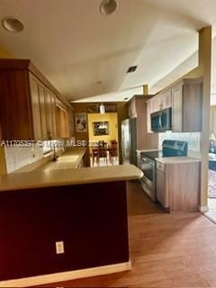 kitchen with kitchen peninsula, appliances with stainless steel finishes, lofted ceiling, and wood-type flooring