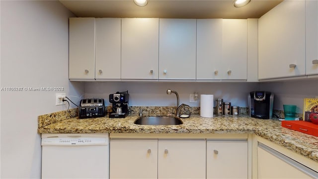 kitchen with light stone countertops, dishwasher, white cabinets, and sink