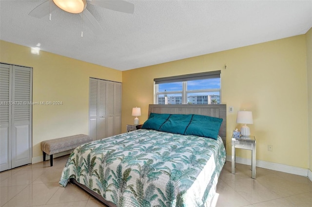 bedroom featuring ceiling fan, light tile patterned flooring, a textured ceiling, and two closets