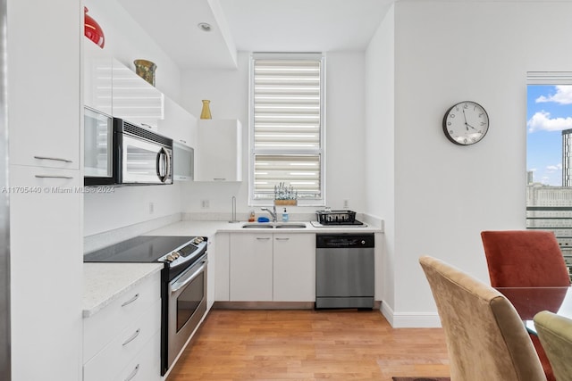 kitchen with sink, stainless steel appliances, light stone counters, light hardwood / wood-style floors, and white cabinets