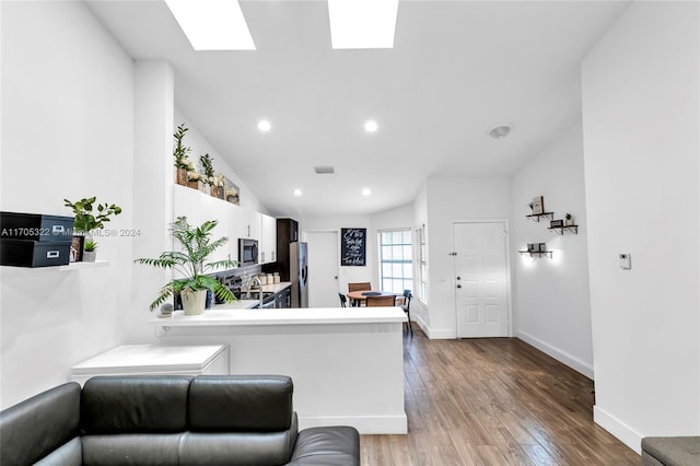 kitchen featuring hardwood / wood-style floors, kitchen peninsula, appliances with stainless steel finishes, and lofted ceiling with skylight