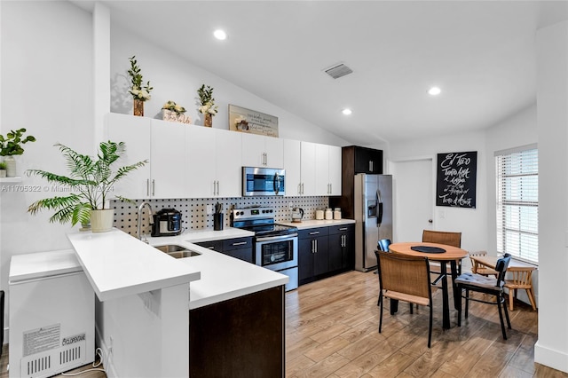 kitchen featuring sink, vaulted ceiling, appliances with stainless steel finishes, light hardwood / wood-style floors, and white cabinetry