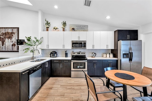 kitchen featuring stainless steel appliances, lofted ceiling with skylight, sink, white cabinets, and light hardwood / wood-style floors