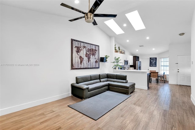 living room featuring a skylight, light hardwood / wood-style floors, high vaulted ceiling, and ceiling fan