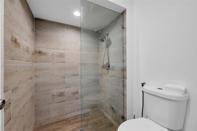 bathroom with tiled shower, hardwood / wood-style floors, and toilet