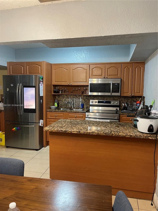 kitchen with sink, backsplash, dark stone counters, light tile patterned flooring, and appliances with stainless steel finishes