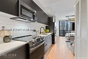 kitchen featuring sink, light wood-type flooring, stainless steel appliances, and backsplash