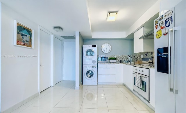 kitchen with white cabinets, stacked washer / drying machine, light tile patterned flooring, and appliances with stainless steel finishes