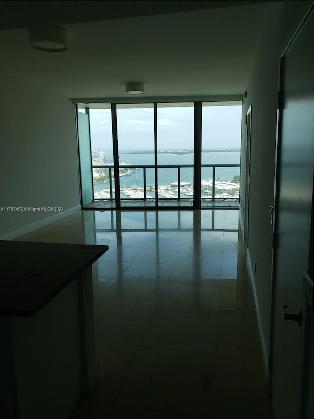 empty room with expansive windows, a water view, tile patterned floors, and plenty of natural light