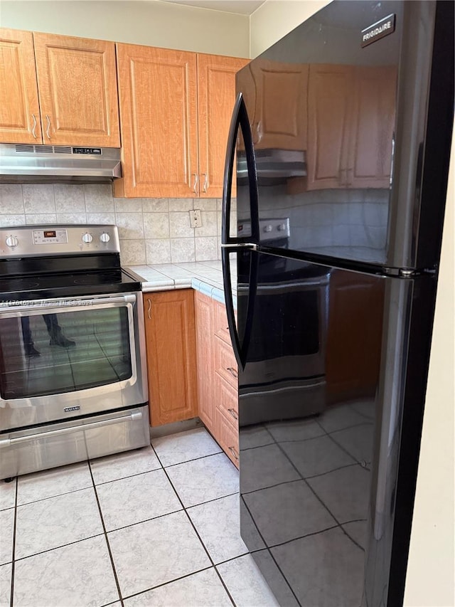 kitchen with light tile patterned floors, backsplash, black fridge, and electric stove