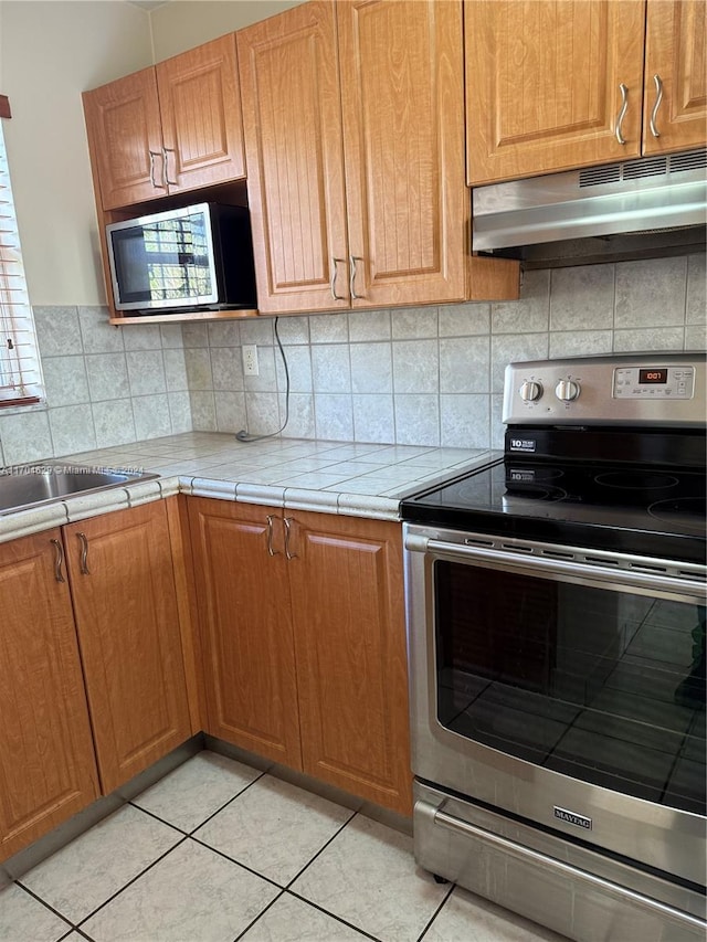 kitchen with sink, tile counters, tasteful backsplash, light tile patterned floors, and appliances with stainless steel finishes