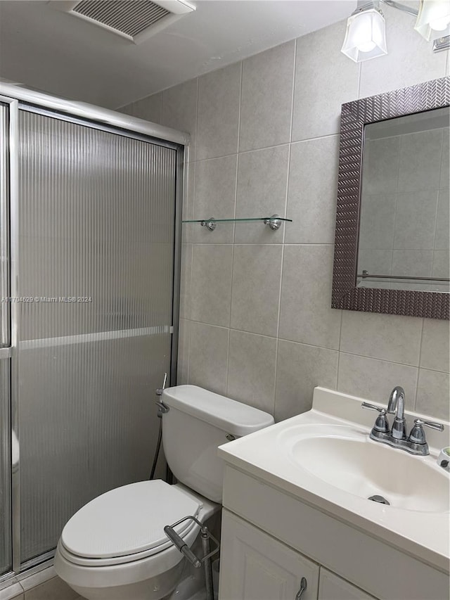 bathroom featuring vanity, decorative backsplash, toilet, tile walls, and an enclosed shower