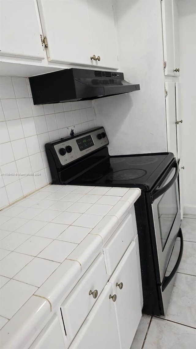 kitchen featuring electric range, tile counters, range hood, decorative backsplash, and white cabinets