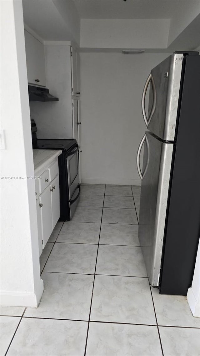 kitchen featuring stainless steel fridge, light tile patterned floors, white cabinetry, and black range with electric stovetop