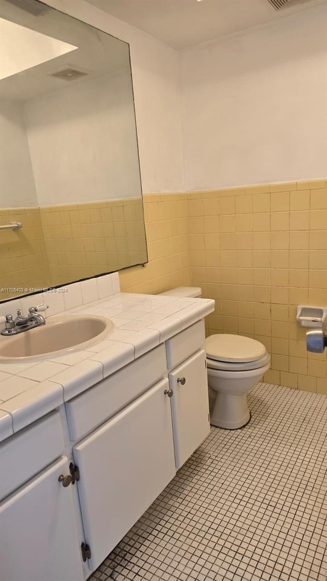 bathroom featuring tile patterned flooring, vanity, toilet, and tile walls