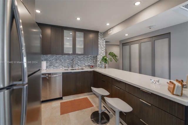 kitchen featuring dark brown cabinetry, sink, tasteful backsplash, kitchen peninsula, and appliances with stainless steel finishes