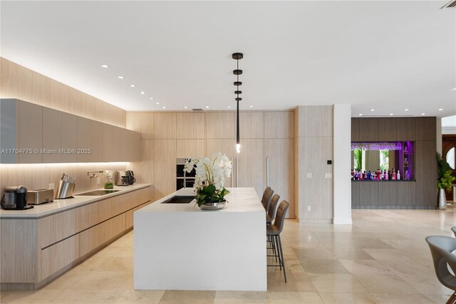 kitchen with pendant lighting, wood walls, a center island with sink, sink, and light brown cabinetry