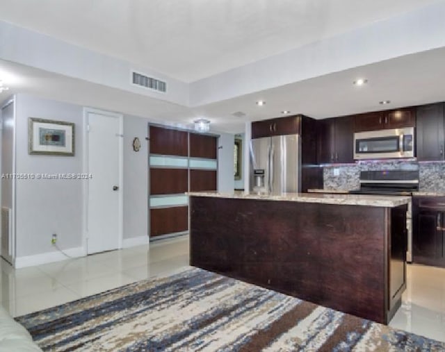 kitchen featuring a center island, decorative backsplash, light stone countertops, dark brown cabinets, and stainless steel appliances