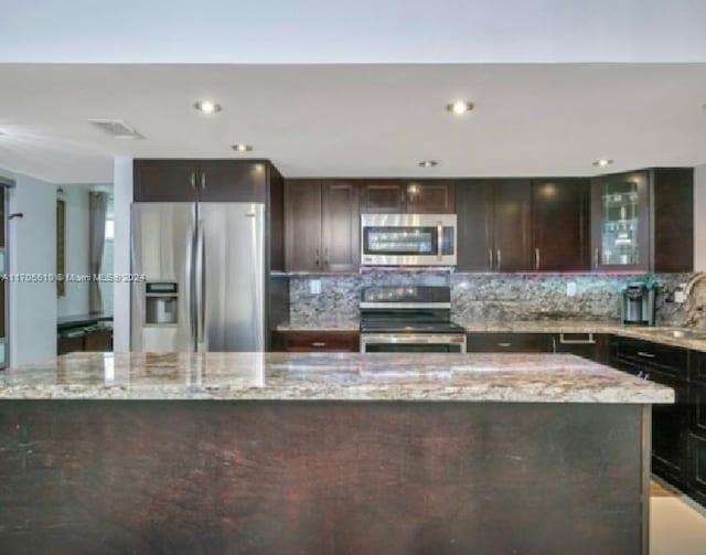 kitchen with backsplash, light stone countertops, dark brown cabinetry, and stainless steel appliances